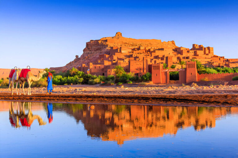 Scenic view of Ait Ben-Haddou with camels and reflection in water.