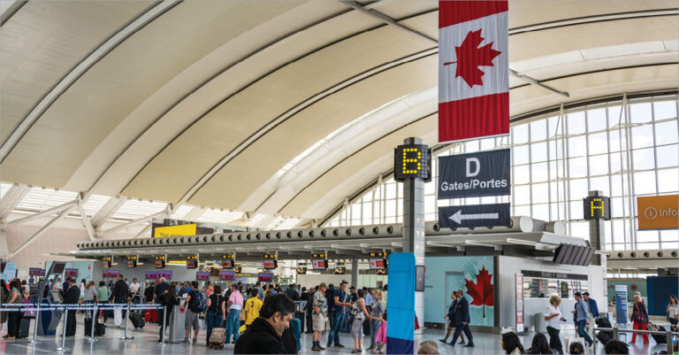 Passengers at Toronto airport terminal with Canadian flag.