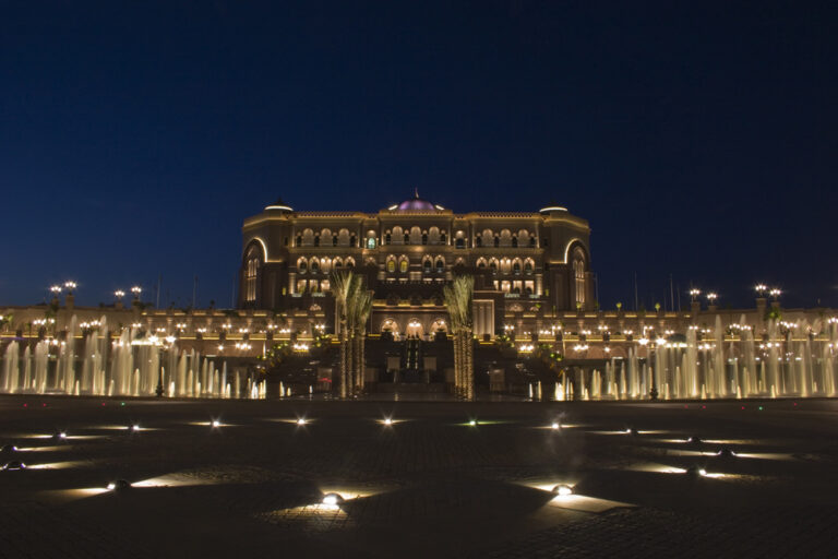 Emirates Palace illuminated at night with fountains.