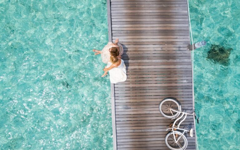 Person sitting on a pier with a bicycle over clear ocean water.