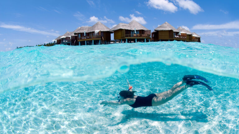 Snorkeler swimming near overwater bungalows in Maldives.