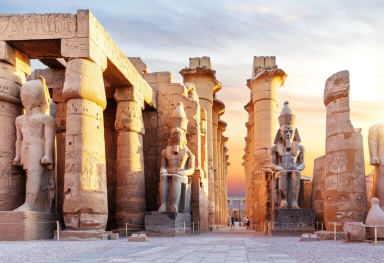 Luxor Temple at sunset with ancient statues and columns.