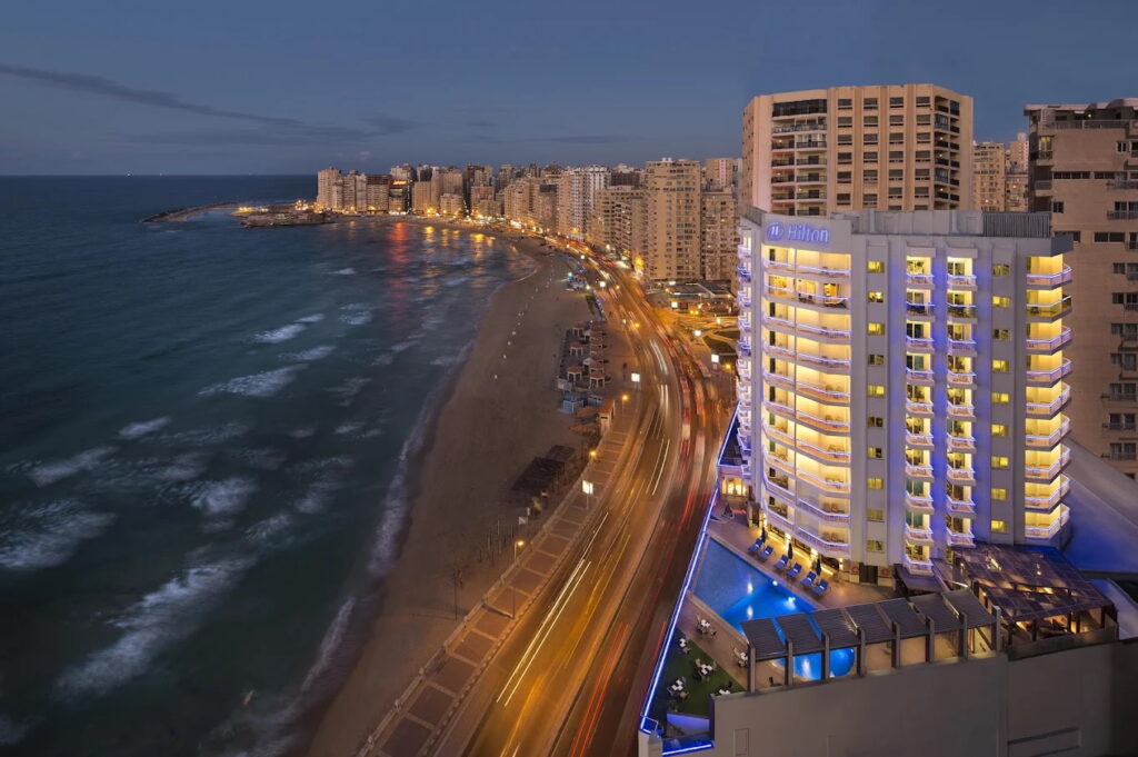 Hilton Alexandria Corniche Hotel at night with city lights and beach view