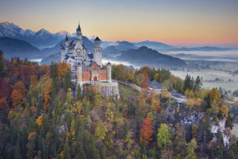 Neuschwanstein Castle in autumn surrounded by colorful trees and mountains.