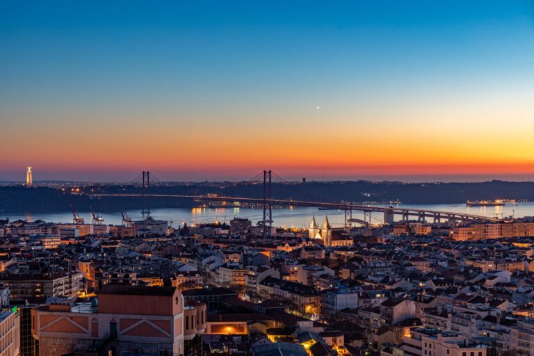 Lisbon sunset with 25 de Abril Bridge and Cristo Rei statue.