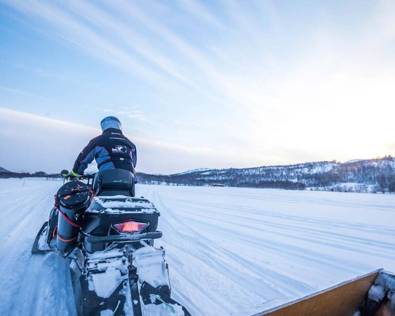 Person riding a snowmobile in a snowy Arctic landscape