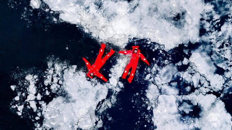 Two travelers floating in survival suits on Arctic ice.