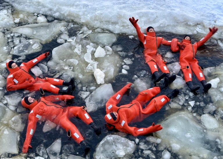 Travelers in survival suits floating among Arctic ice.