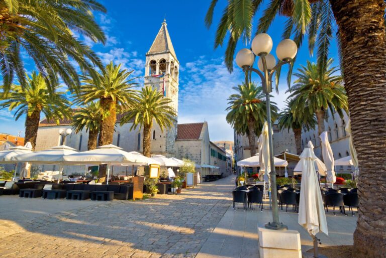 Historic street with palm trees and outdoor cafes in Trogir, Croatia