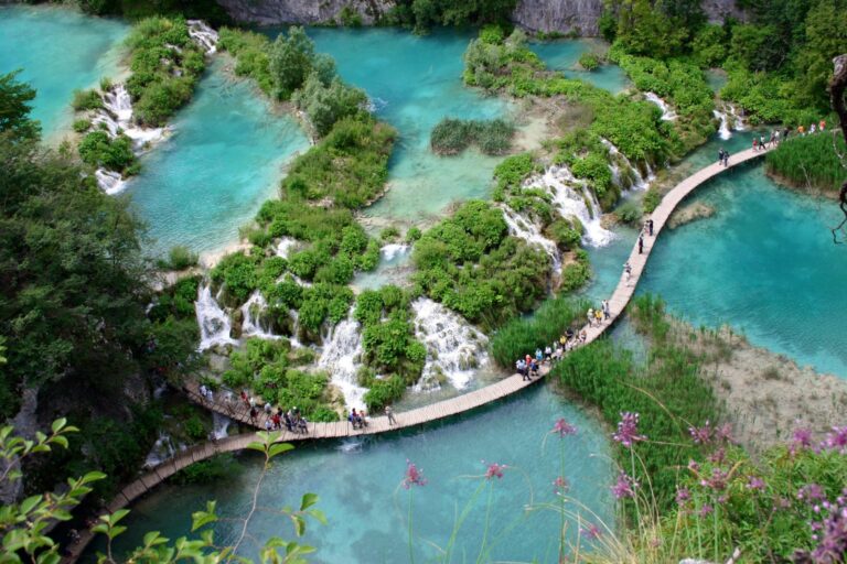 Tourists walking on boardwalks over turquoise lakes in Plitvice National Park.