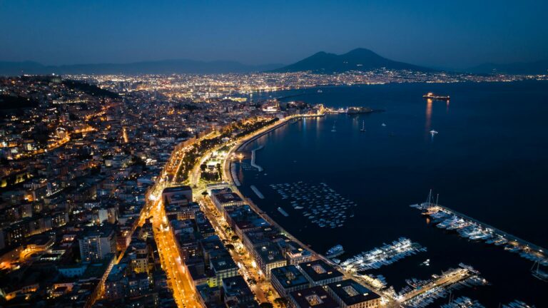 Aerial view of Naples coastline at night with city lights and Mount Vesuvius.
