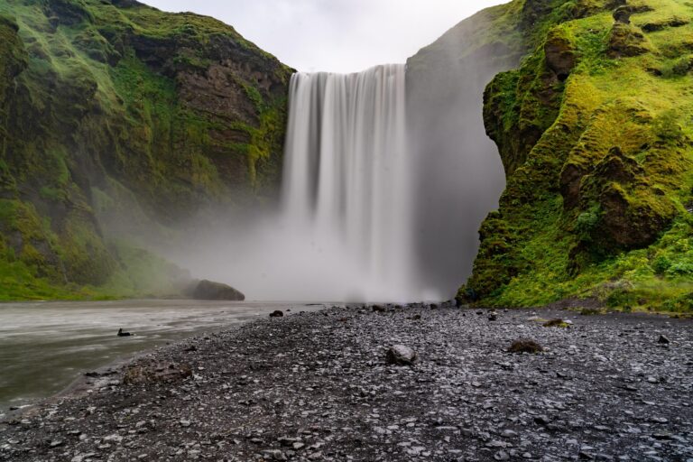 Skogafoss waterfall in Iceland surrounded by lush green cliffs.
