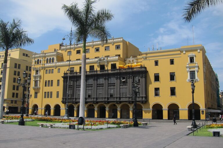 Historic yellow building in Plaza Mayor, Lima with palm trees.