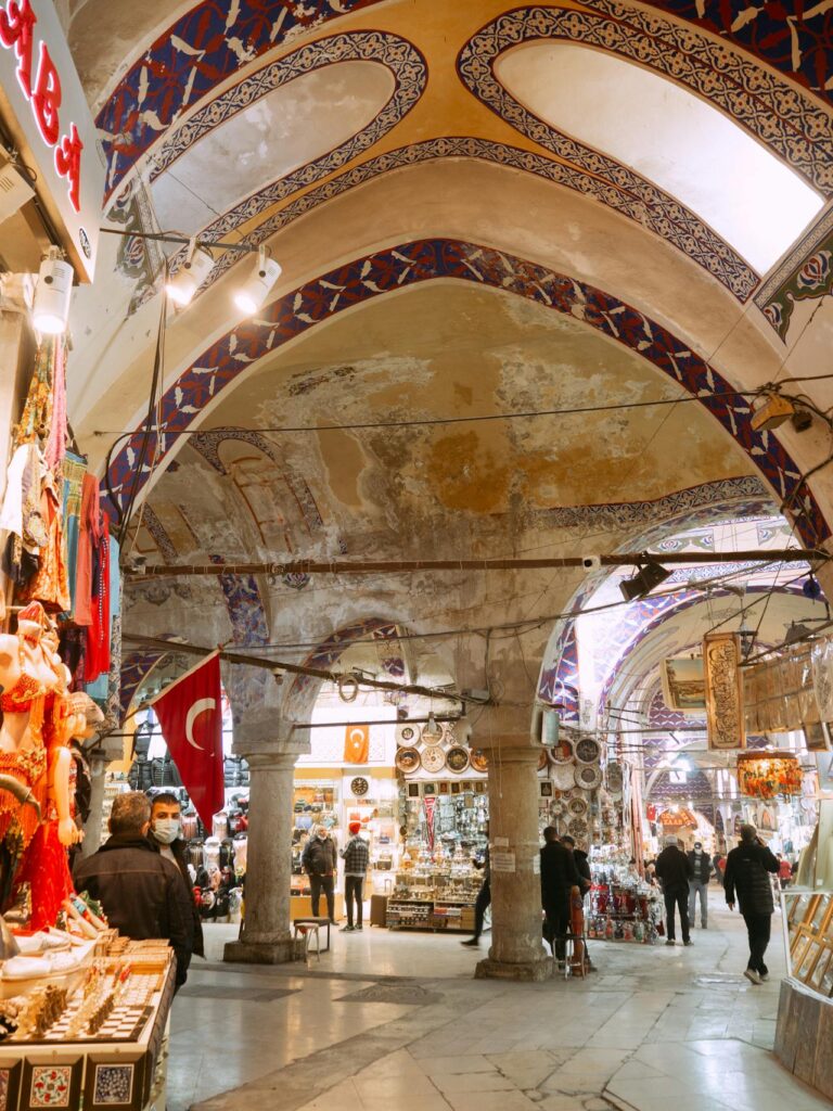 Interior view of the Grand Bazaar in Istanbul with shoppers and Turkish flags.
